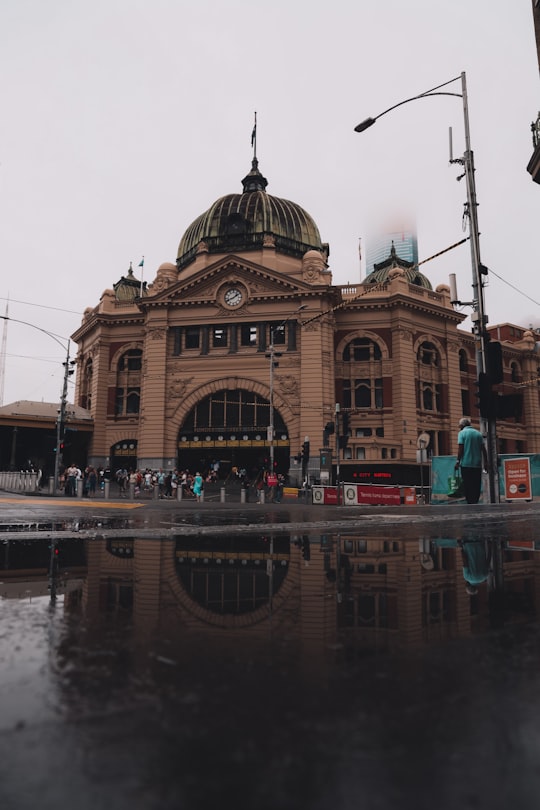 brown and beige concrete building near body of water during daytime in Flinders Street railway station Australia