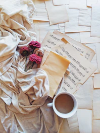 A pastel-toned flat lay of a journal, delicate flowers, and a cup of tea on a light wooden table.