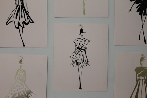 The image contains a series of fashion sketches displayed on a wall. Each sketch features abstract, stylistic drawings of women in various fashionable dresses. The artwork is monochromatic and uses a minimalistic design approach.