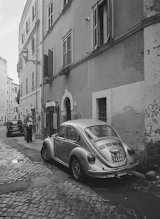 A narrow cobblestone street in Rome with a small car parked near ancient ruins.