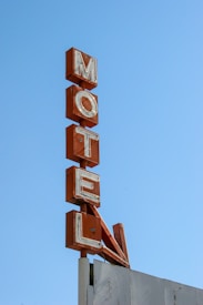 An old, weathered motel sign with large, red letters stacked vertically against a clear blue sky.