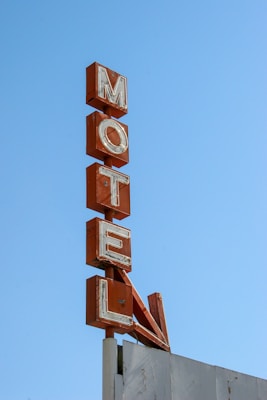 An old, weathered motel sign with large, red letters stacked vertically against a clear blue sky.