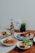 A collection of dishes is beautifully arranged on a wooden table, including a plate with blue rice and roasted chicken, a bowl with cooked prawns garnished with herbs, a bowl of mixed vegetables, and a dish with sliced omelet and fresh greens. There is a bottle of beer labeled 'Tiger Crystal,' a small potted plant, and a card that reads 'happy father's day.'