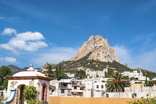 Edificios de hormigón blanco y marrón al fondo se ve Peña de Bernal, durante el día.