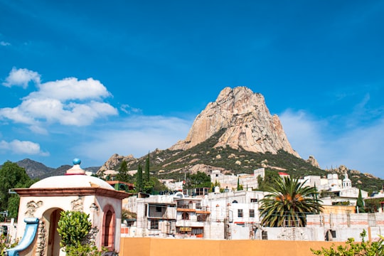 white and brown concrete buildings near green mountain under blue sky during daytime in Peña de Bernal Mexico