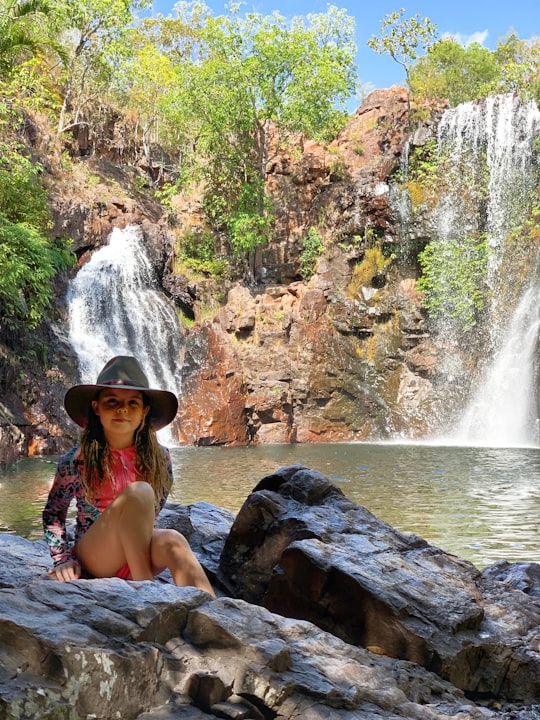 woman in blue and white bikini sitting on rock near waterfalls during daytime in Litchfield National Park Australia