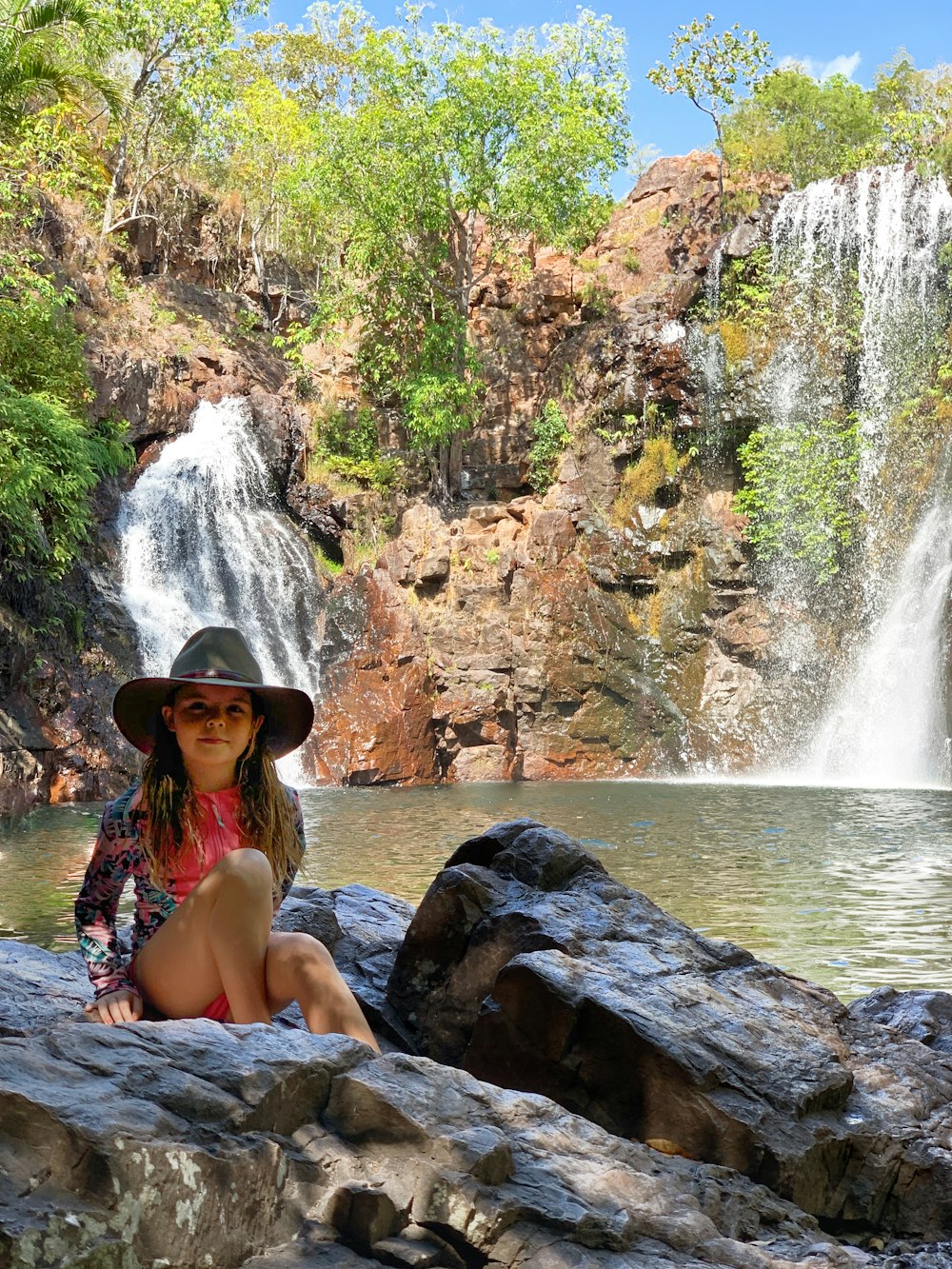 woman in blue and white bikini sitting on rock near waterfalls during daytime