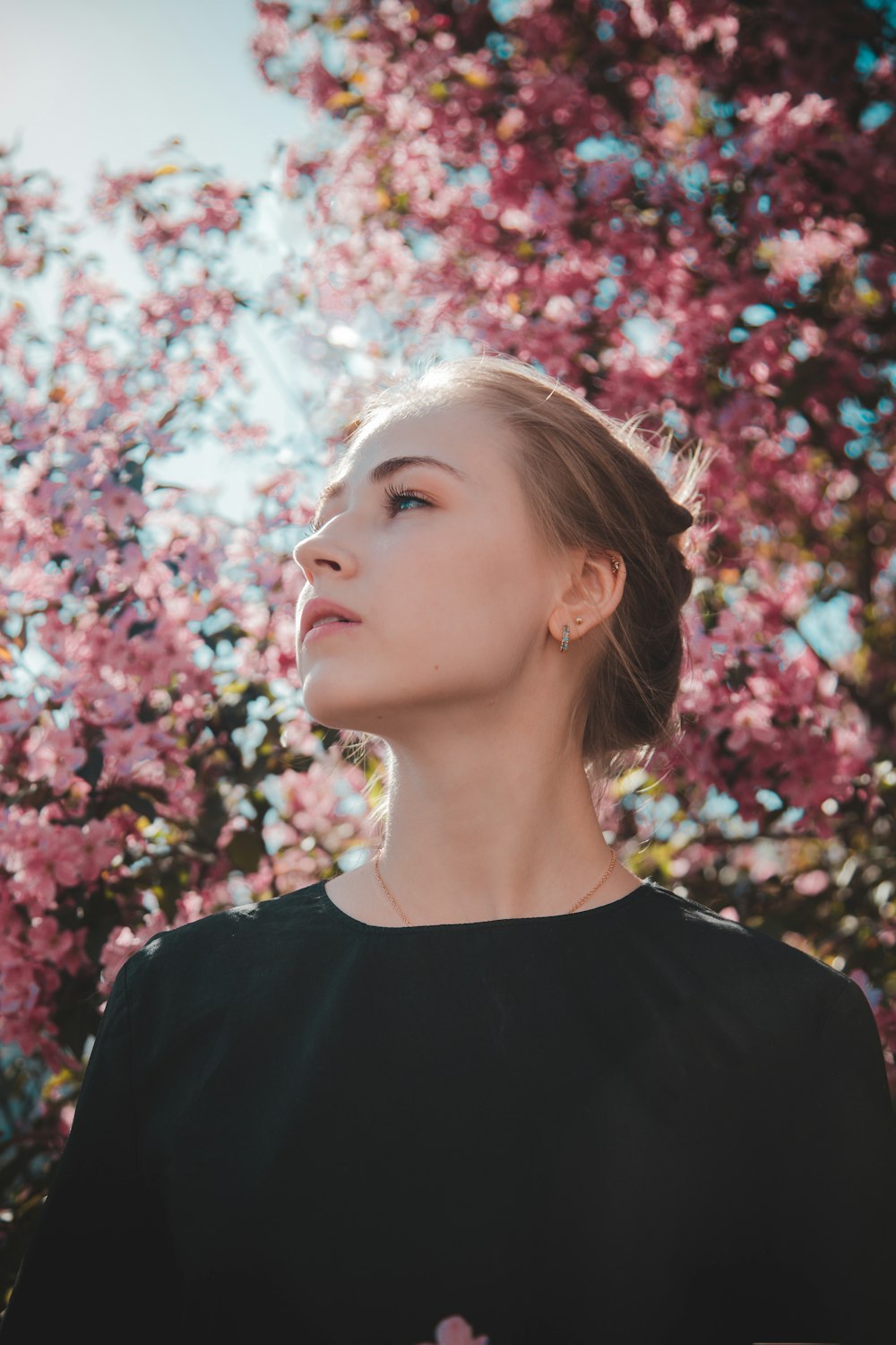 woman in black crew neck shirt standing under pink cherry blossom tree during daytime