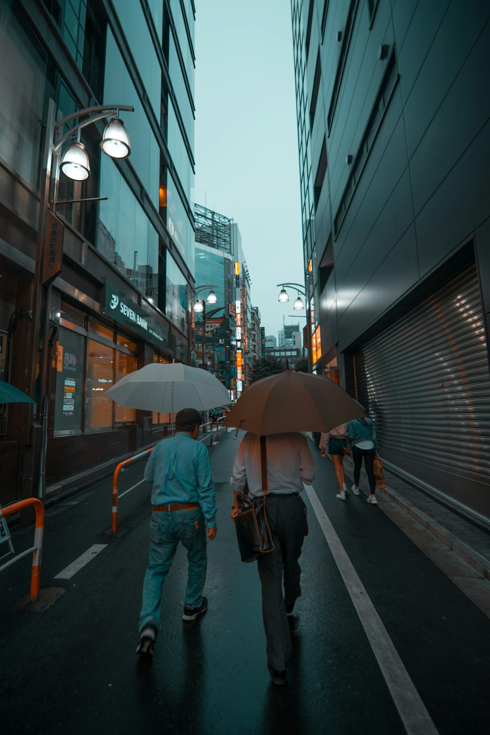 man in blue jacket and blue denim jeans holding umbrella walking on sidewalk during daytime