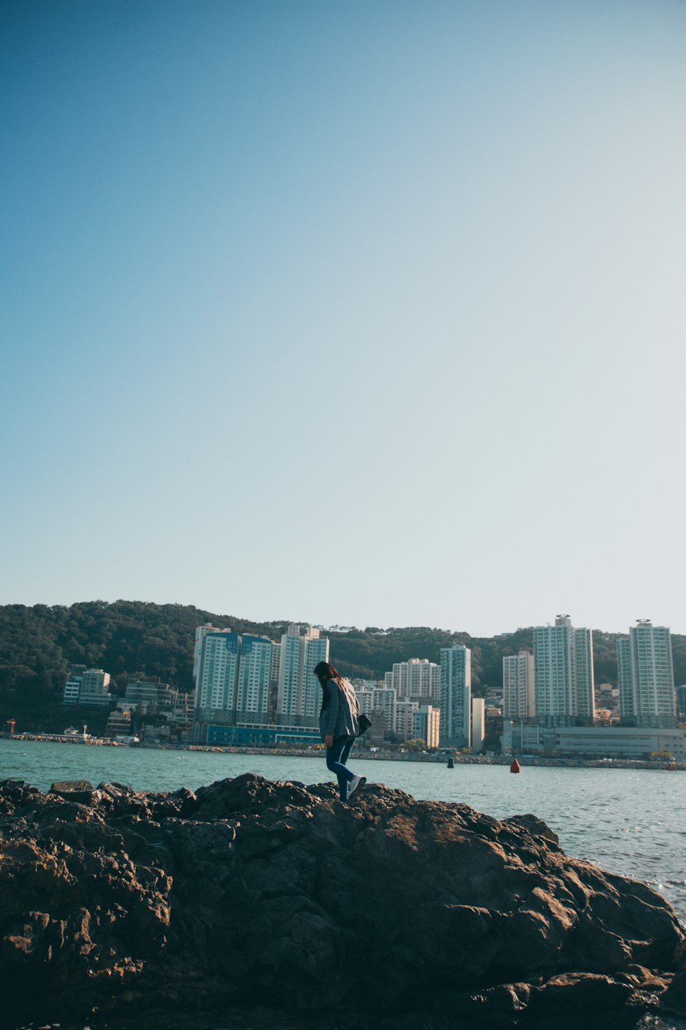 man in black shirt and black pants standing on rock near body of water during daytime