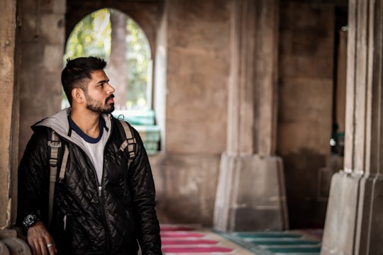 man in black leather jacket sitting on red and white rug in Sidi Saiyyed Mosque India