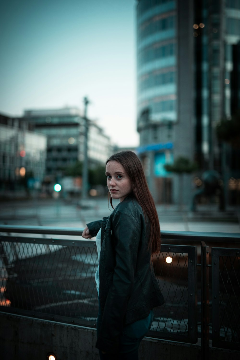 woman in black leather jacket standing on bridge during daytime