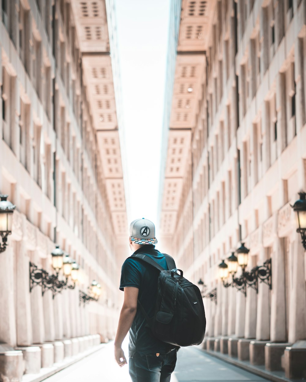 man in black shirt wearing white cap and backpack standing in front of brown concrete building