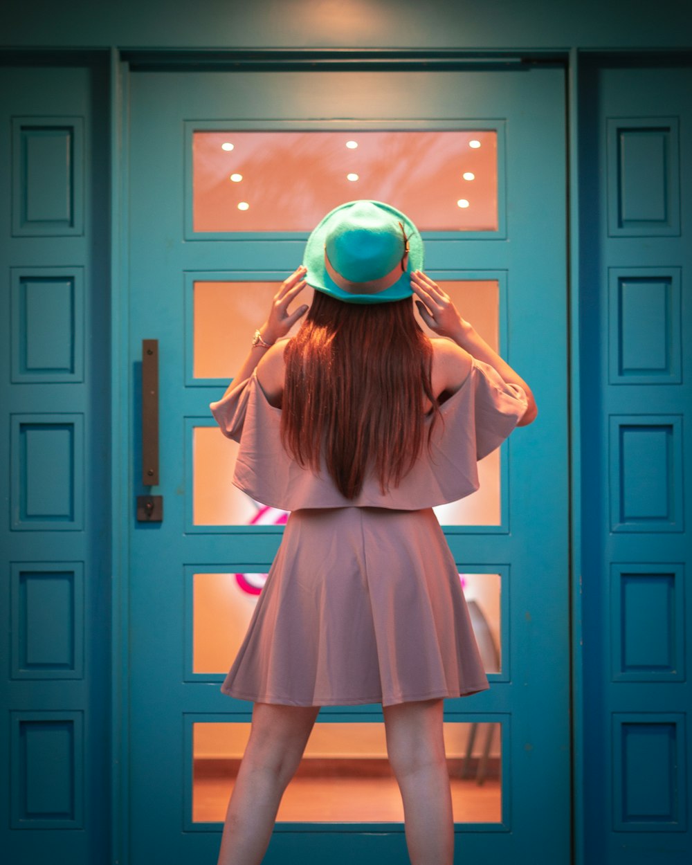 Femme en robe à manches longues marron debout près de la porte en bois rose