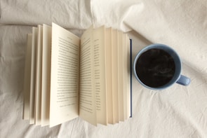 An open book with a steaming cup of coffee beside it.
