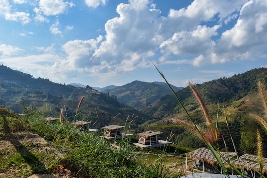 green grass field near mountains under white clouds and blue sky during daytime in Chiang Mai Thailand