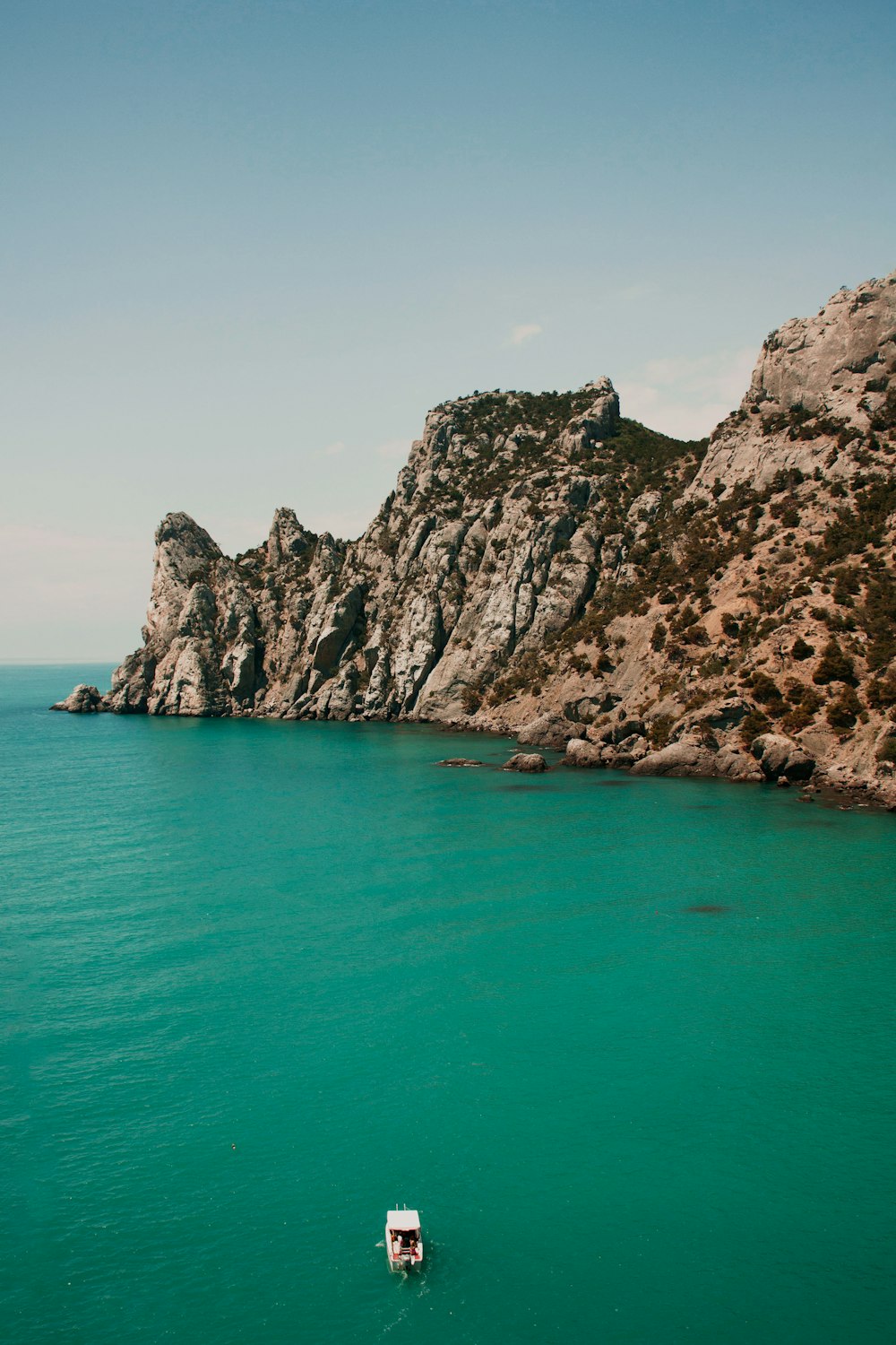 brown rocky mountain beside blue sea under blue sky during daytime