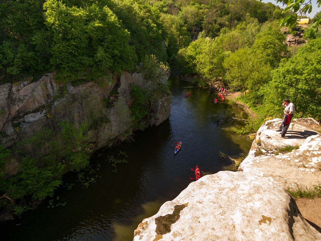 person in red jacket and black pants standing on rock near river during daytime