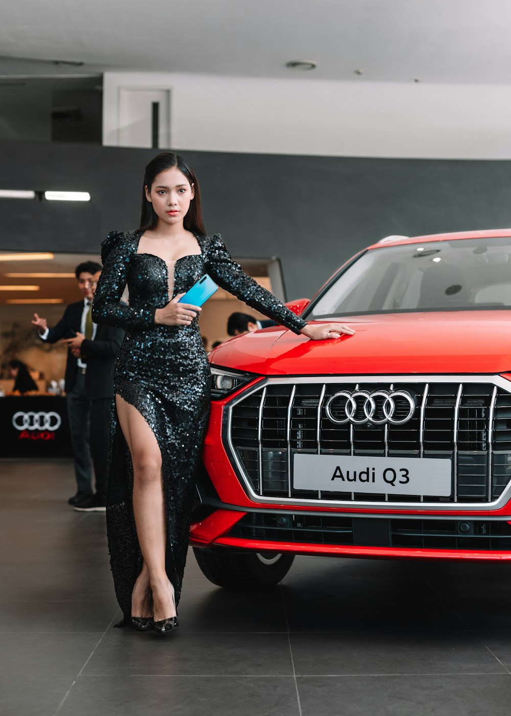 Frau in schwarzem Kleid steht neben rotem Audi Car