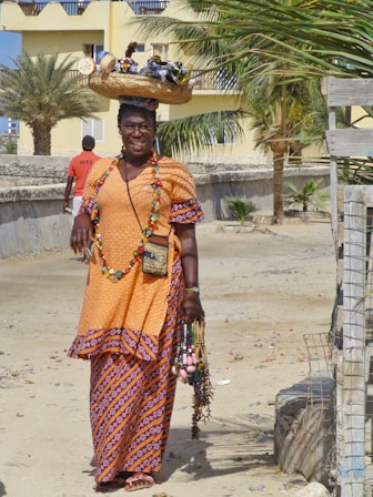 woman in red and yellow sari dress wearing brown woven hat standing on brown sand during