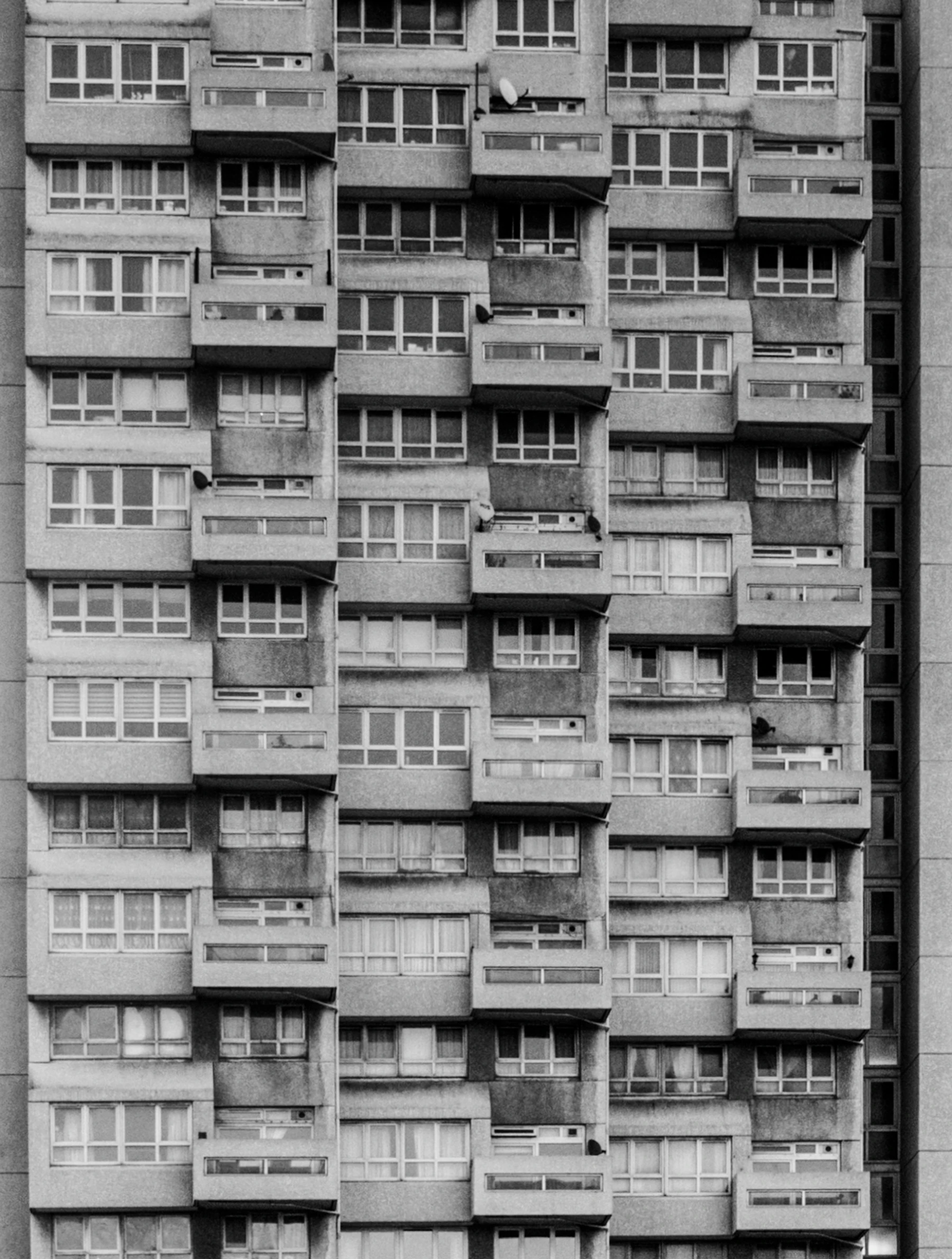 A grey brutalist housing block, balconies stacked in a strict grid