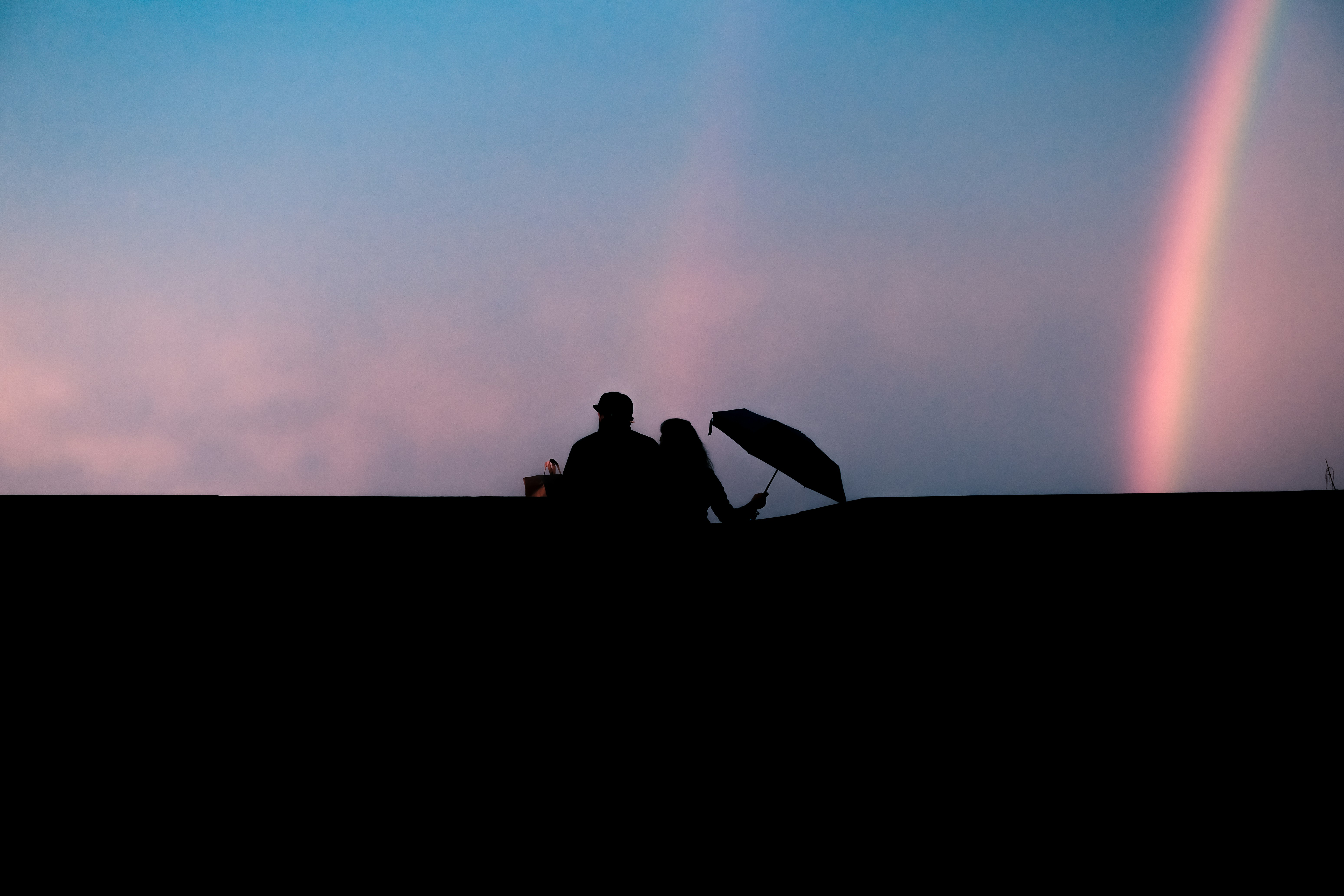 silhouette of man and woman sitting on bench under blue sky during daytime