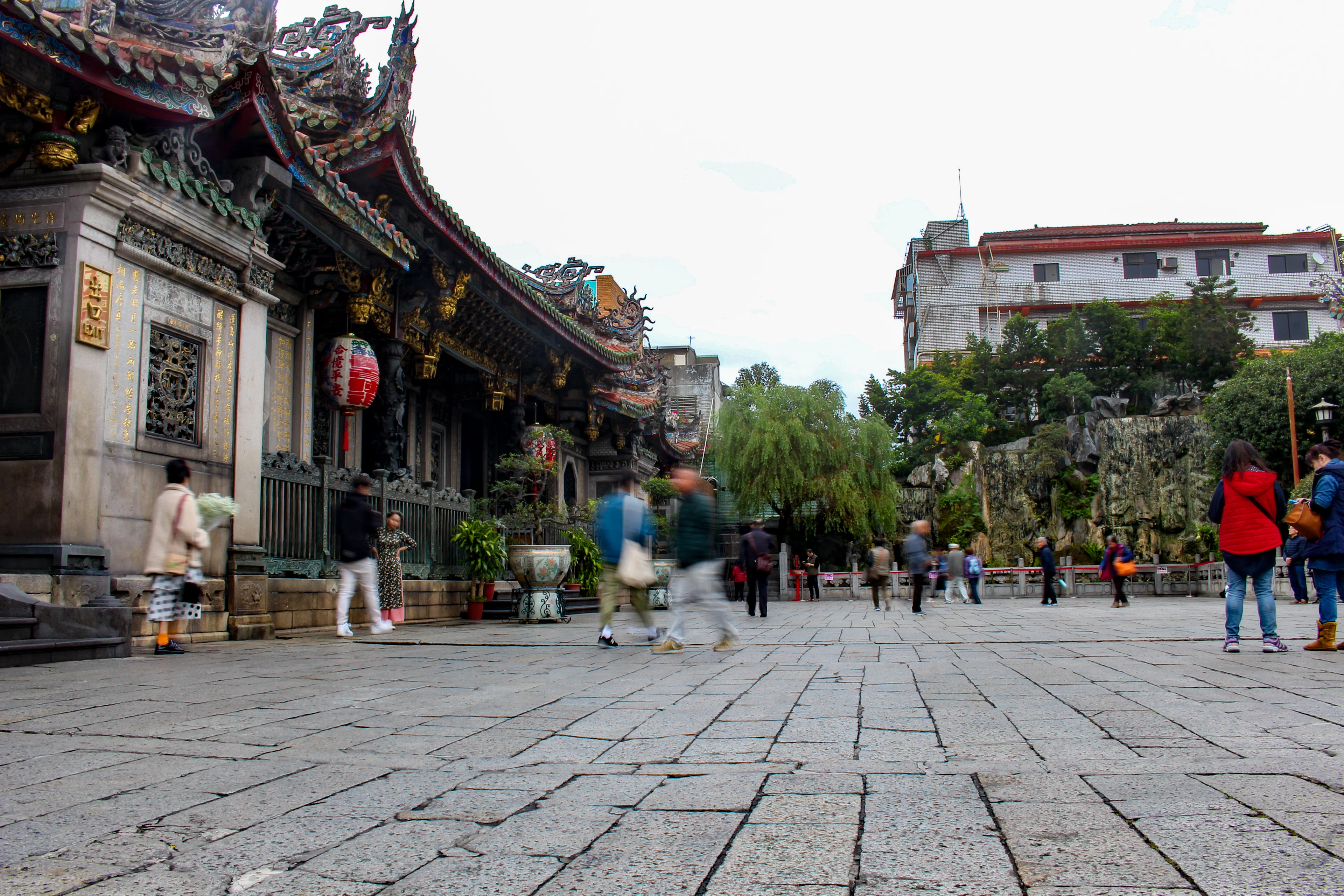 The forecourt of Longshan Temple in Taipei, its carved roofline against a pale sky