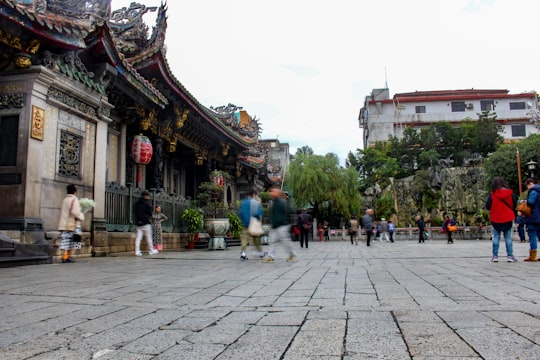 people walking on gray concrete pavement near brown concrete building during daytime in Lungshan Temple Taiwan