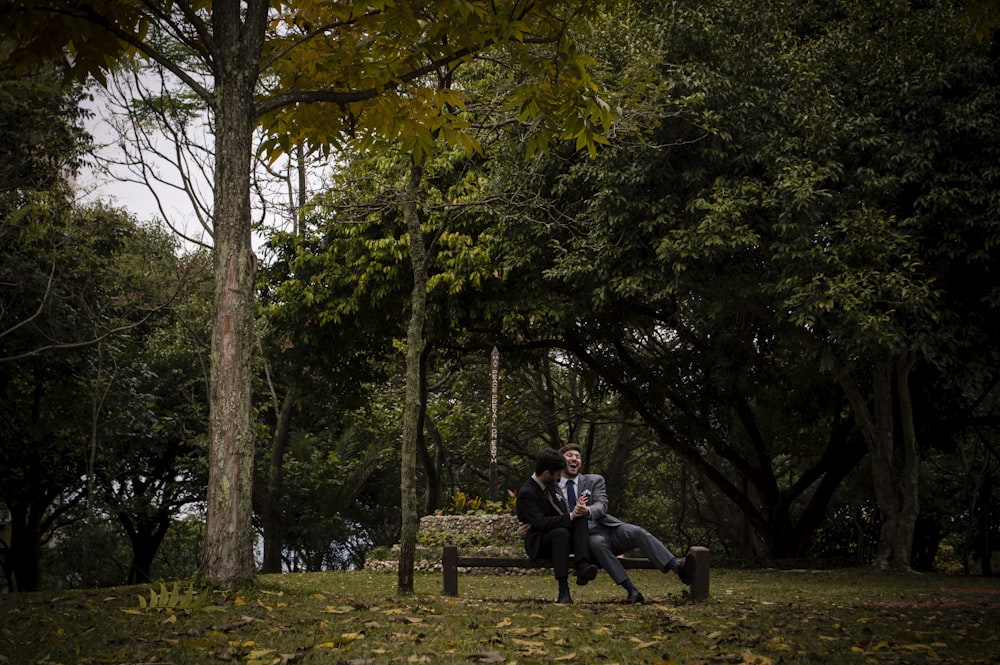 Hombre en chaqueta negra sentado en banco de madera marrón cerca de árboles verdes durante el día