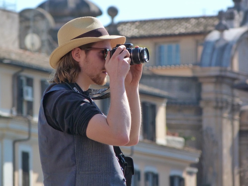 man in black t-shirt and brown fedora hat using black binoculars