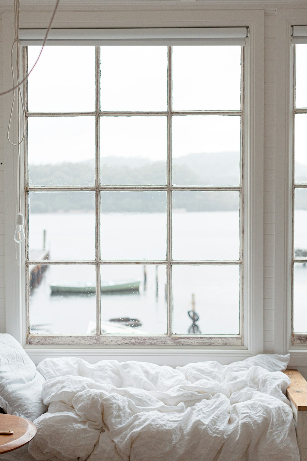 Cama blanca cerca de una ventana de vidrio con marco blanco