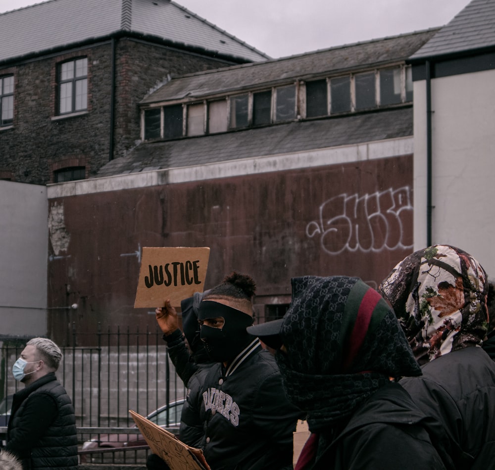 personnes en veste noire debout près d’un mur brun pendant la journée