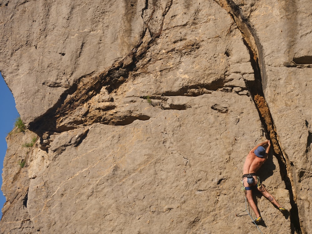 Mujer en camiseta sin mangas azul escalando en la montaña de roca marrón durante el día