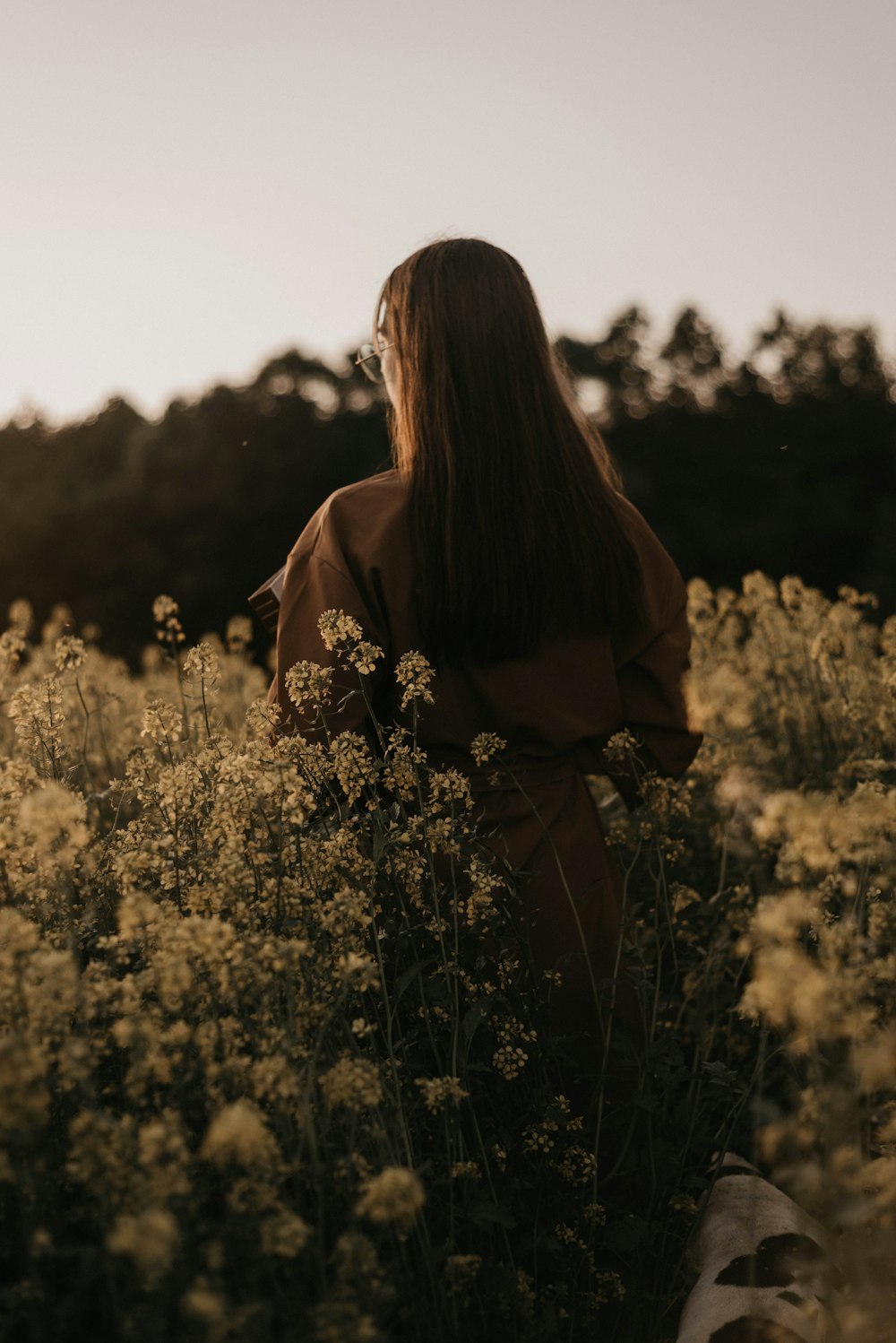 낮 동안 노란 꽃밭에 서 있는 갈색 긴팔 셔츠를 입은 여자