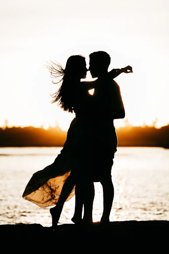 A silhouette of two people embracing against a bright golden light over water