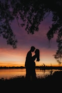Sunset silhouette of couple embracing by a peaceful lake.