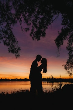 Sunset silhouette of couple embracing by a peaceful lake.