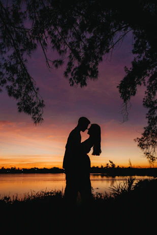 Couple enjoying a romantic sunset by a calm lake surrounded by trees.