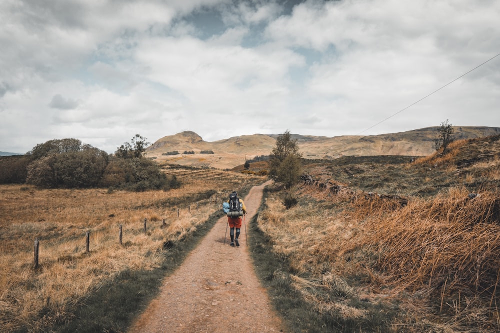 Persona con chaqueta roja caminando por un camino de tierra marrón durante el día
