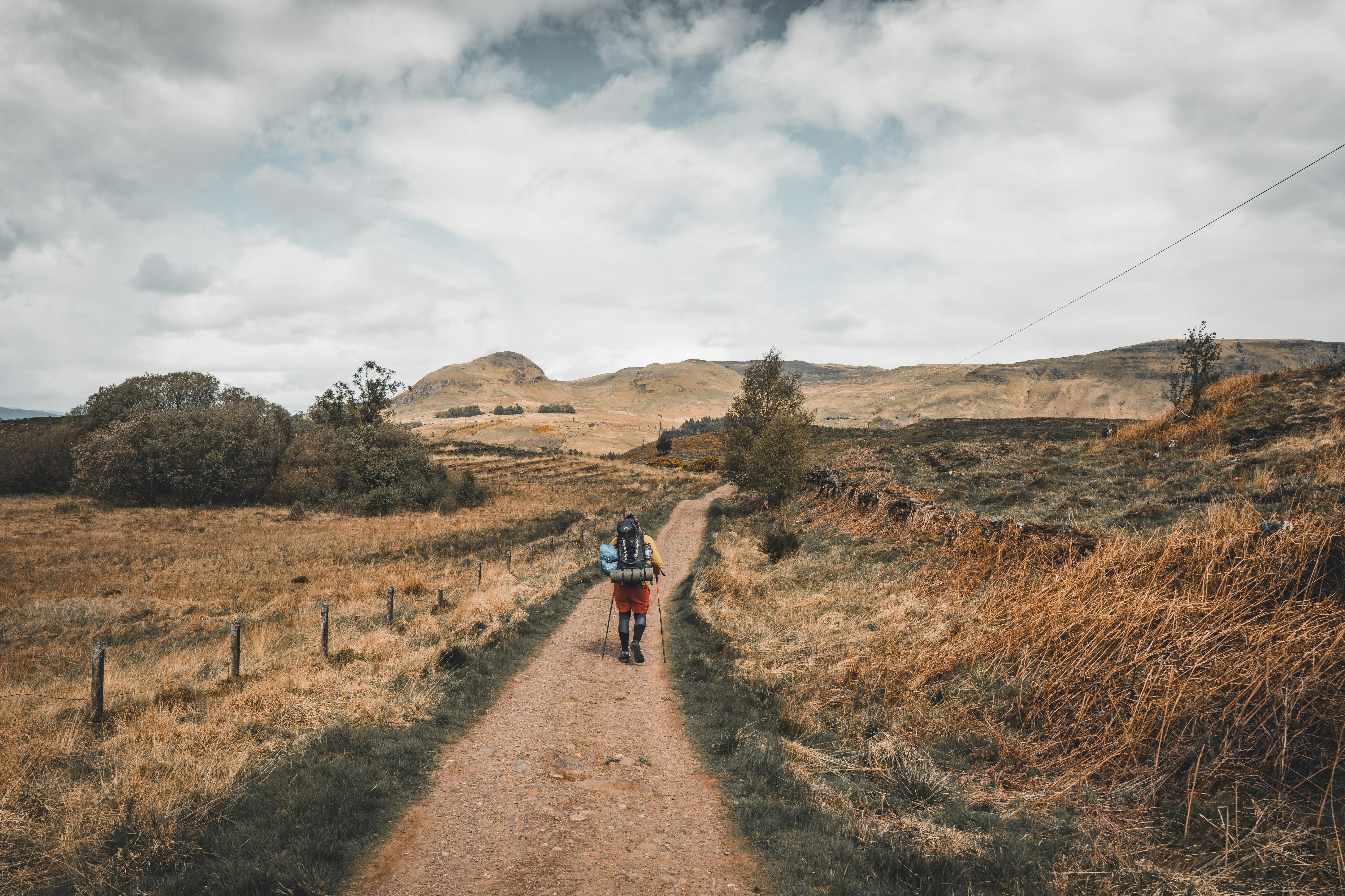 person in red jacket walking on brown dirt road during daytime