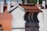 A close-up view of a chimney with a red tiled roof against a backdrop of similar architectural structures. The chimney is made of light-colored bricks, and the tiles are neatly aligned. The background is slightly blurred, highlighting the focus on the chimney.