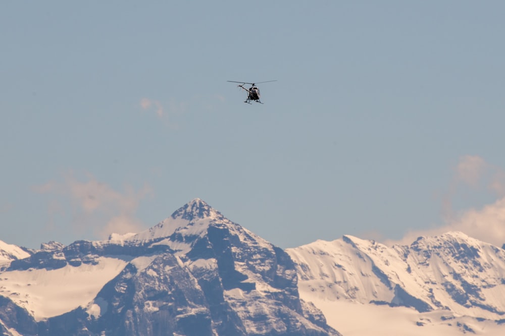 black helicopter flying over snow covered mountain during daytime