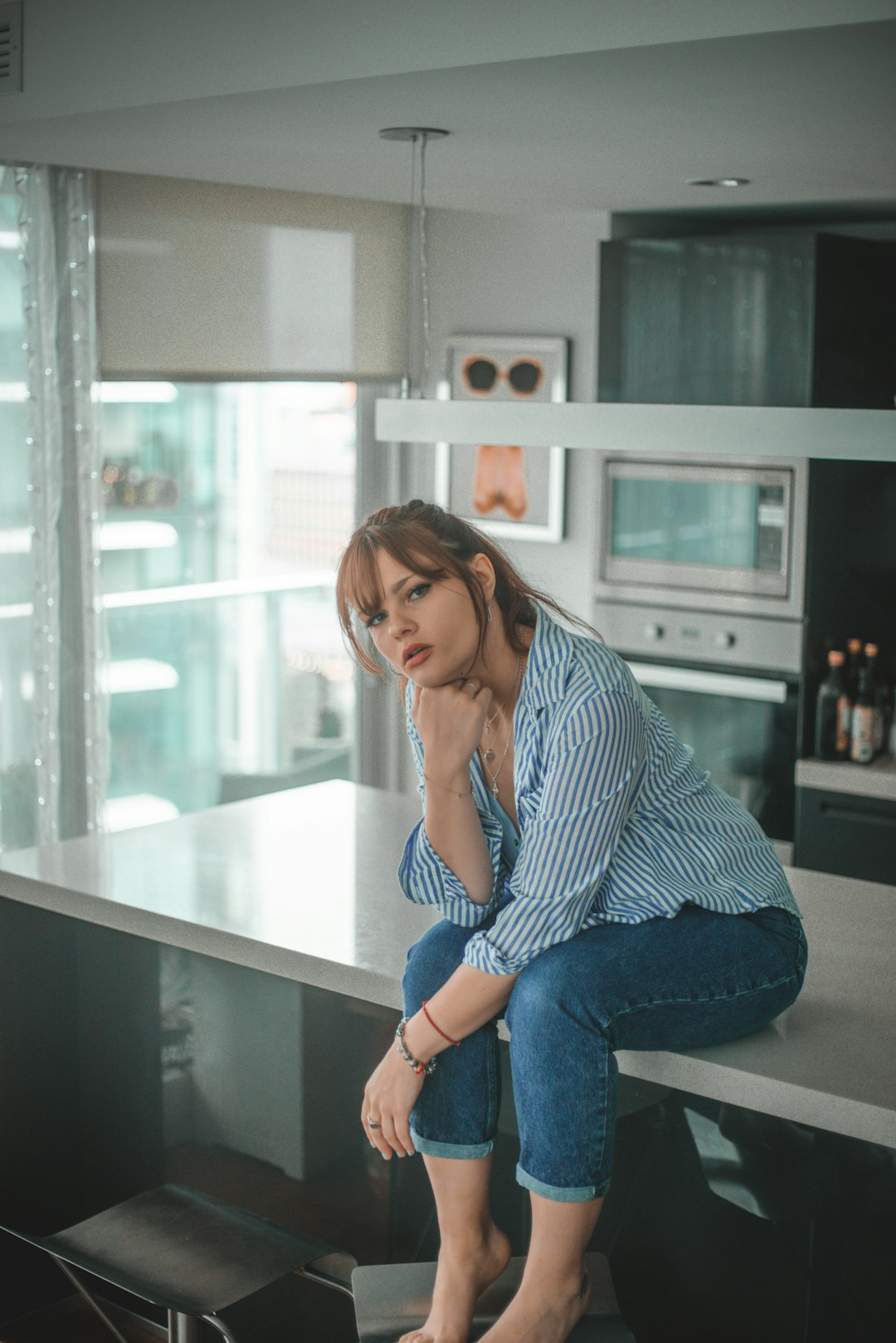 woman in blue and white striped long sleeve shirt and blue denim jeans sitting on white