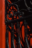 An ornamental wrought iron gate with intricate swirl patterns casts bold shadows against a vibrant red background, creating an artistic interplay of light and texture.
