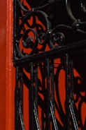 An ornamental wrought iron gate with intricate swirl patterns casts bold shadows against a vibrant red background, creating an artistic interplay of light and texture.