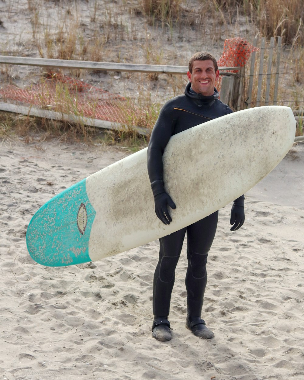 man in black wet suit holding white surfboard