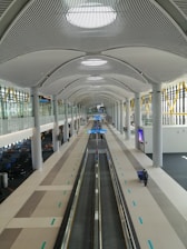 Modern airport terminal with travelers walking and planes visible outside large windows.