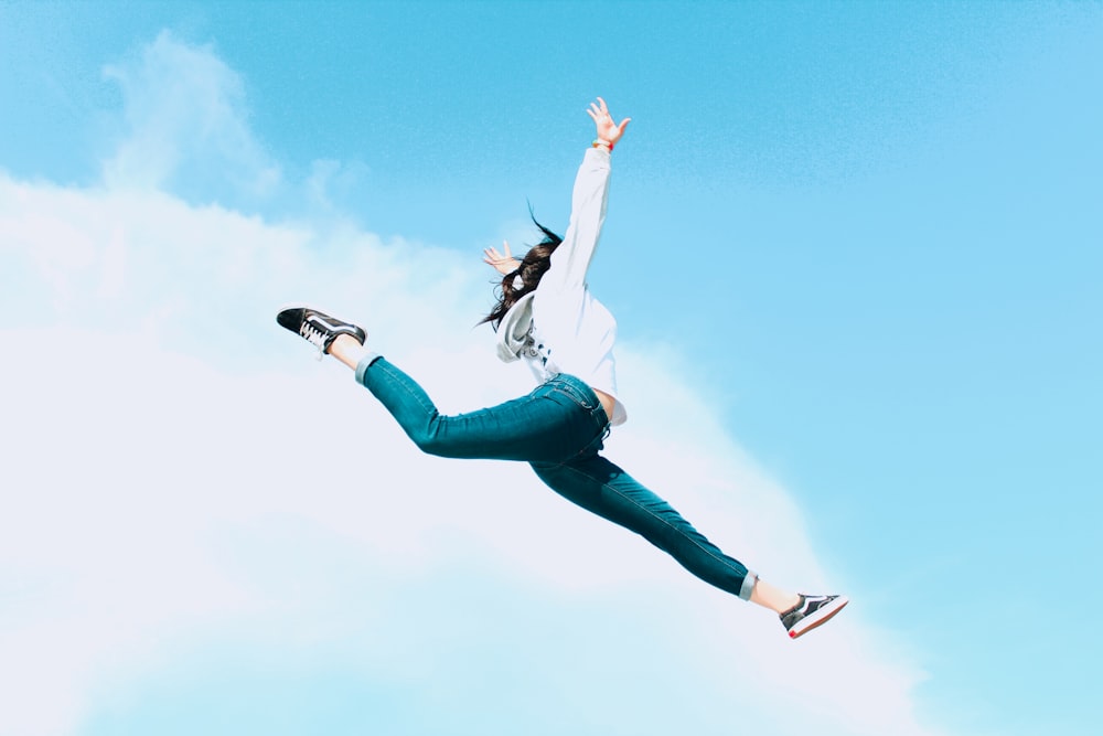 白いシャツとブルーデニムのジーンズを着た女性が昼間の青空の下を飛び跳ねる