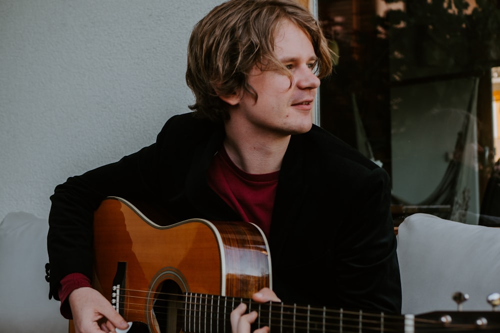 man in black long sleeve shirt playing brown acoustic guitar