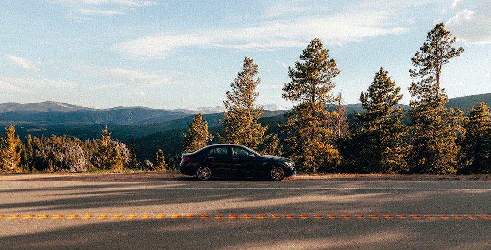 black sedan on road near green trees during daytime